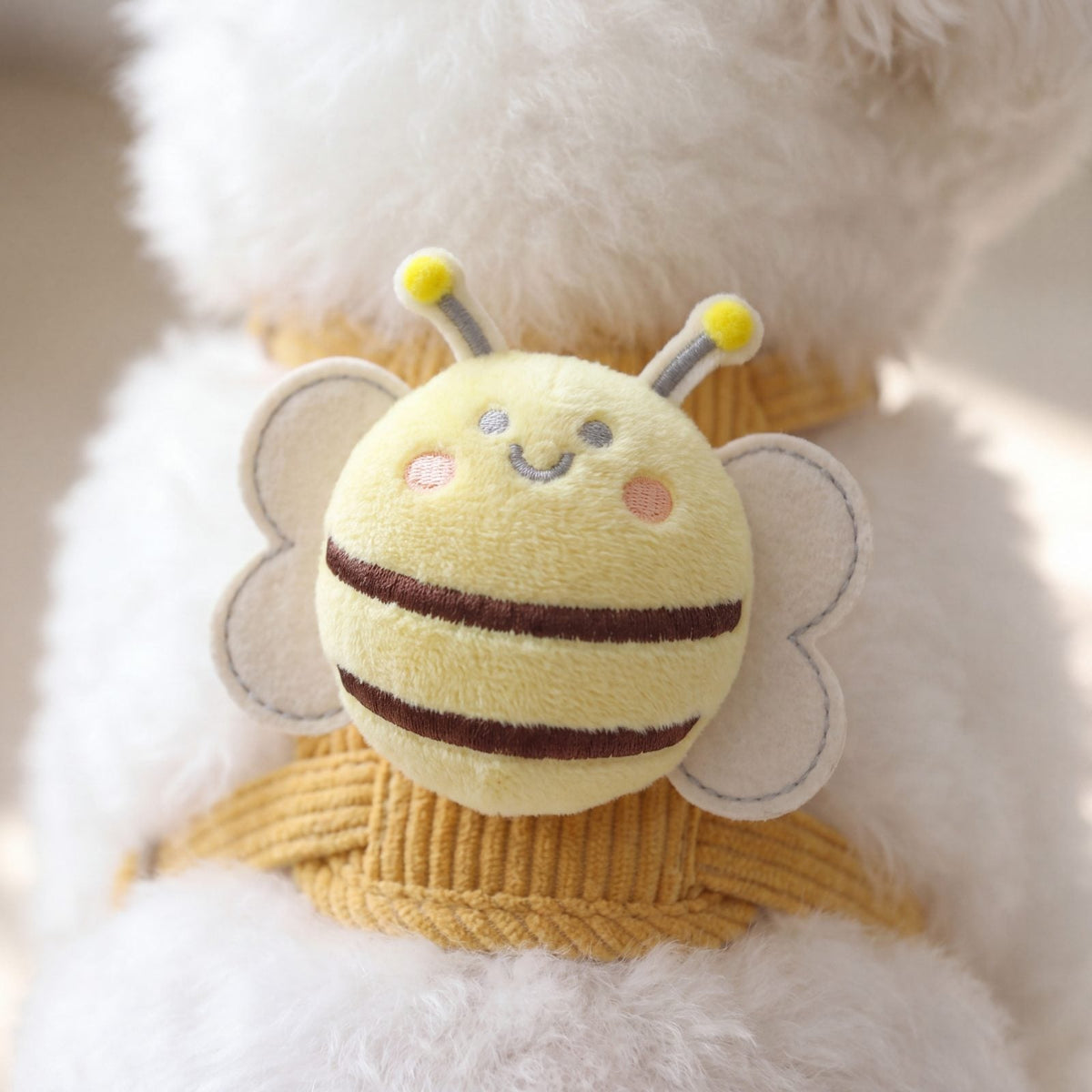 Gros plan sur l'abeille en peluche du harnais petit chien jaune, avec ses rayures marron, ses ailes crème et ses antennes à pompons jaunes
