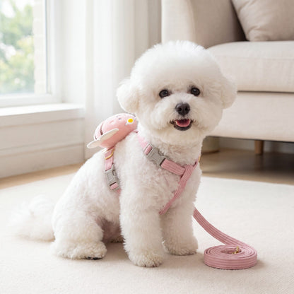 Bichon blanc assis de face portant le harnais abeille 3D rose avec sa laisse assortie dans un salon lumineux