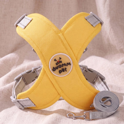 Harnais croisé en X jaune moutarde avec sa laisse grise, présenté sur un tissu beige