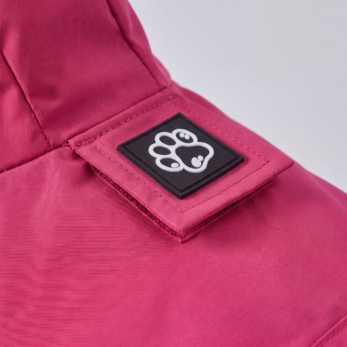 Gros plan sur l'écusson noir à empreinte de patte cousu à l'arrière de la capuche de l'imperméable rose pour chien