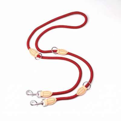 Photographie d'une laisse de chien double multifonctions en corde tressée rouge avec deux mousquetons et trois anneaux métalliques réglables sur un fond blanc. Pliée en forme de S