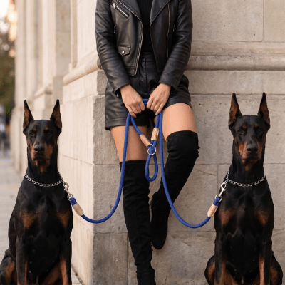 Laisse chien double en corde bleue multifonctions pour promener deux chiens simultanément tenue par une femme avec deux Dobermans