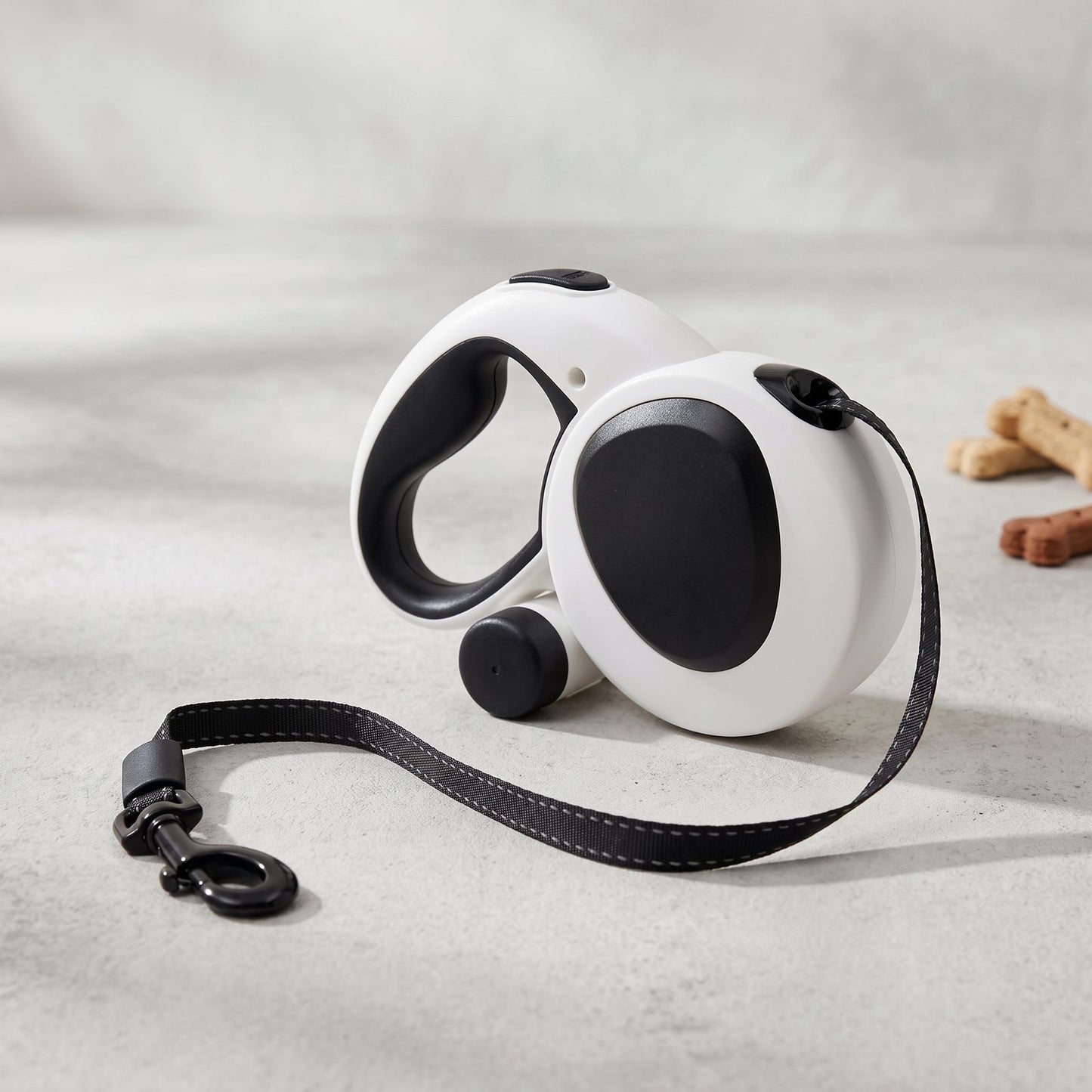 Packshot de la laisse enrouleur 5m pour chien IronTrek, coloris blanc et noir, posée avec des friandises pour chien