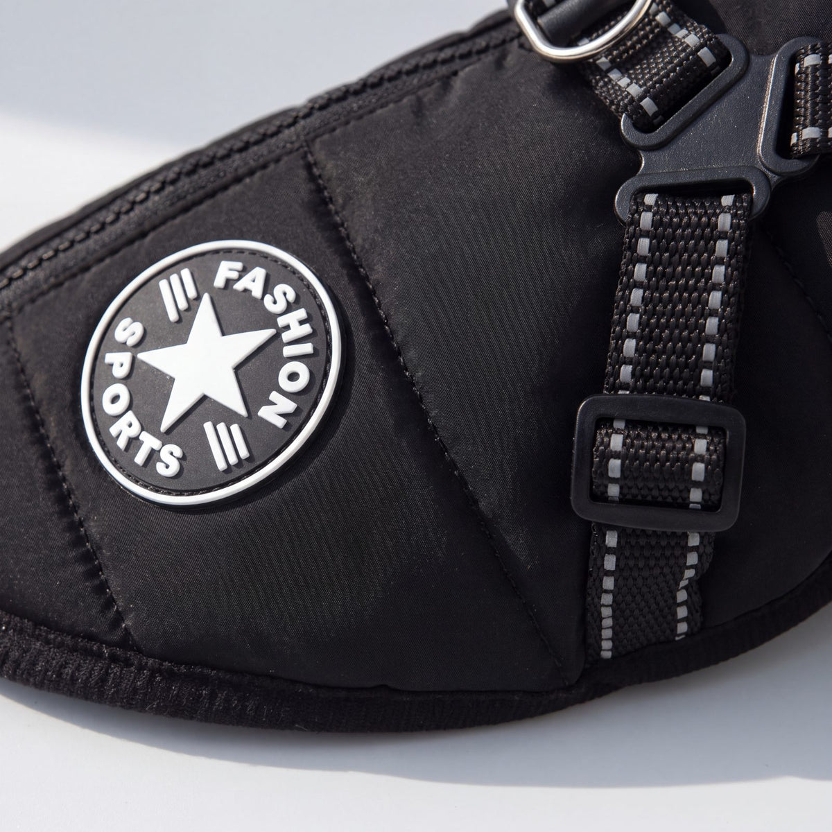 Gros plan sur l'écusson rond Fashion Sports et la sangle réfléchissante du manteau pour chien noir