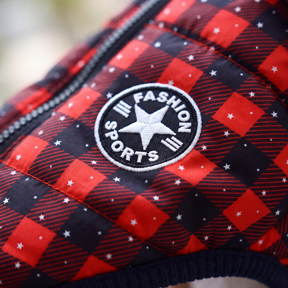 Gros plan sur le motif tartan rouge et noir et l'écusson rond du manteau pour chien