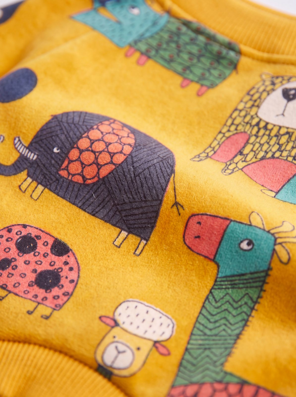 Gros plan sur l'imprimé d'animaux colorés du pull chien jaune : éléphant, coccinelle et girafe
