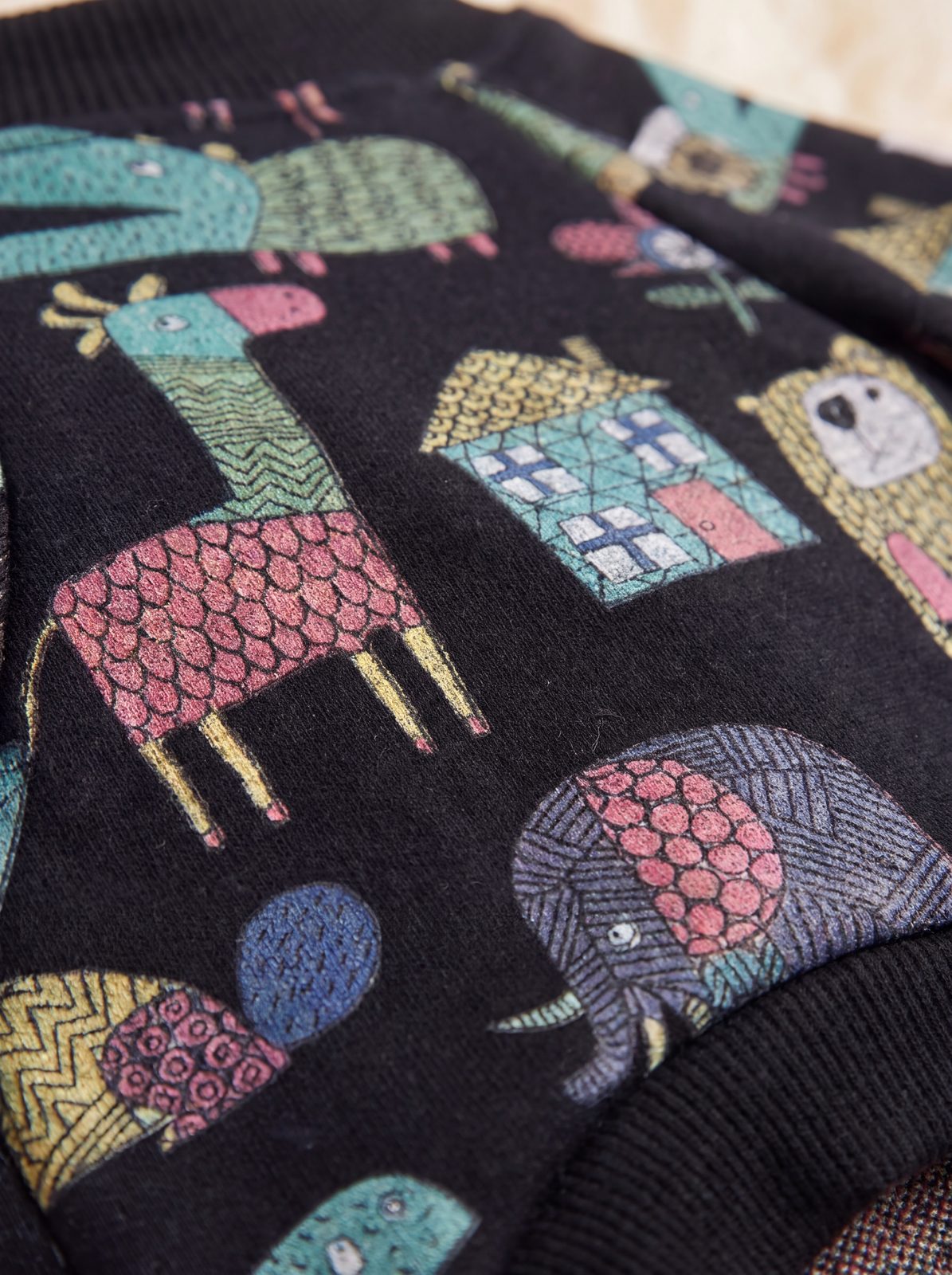 Zoom sur l'imprimé de girafes, d'éléphant et de maisons colorés du pull chien noir doublé polaire