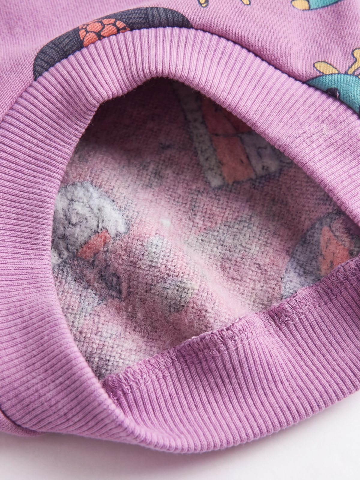 Gros plan sur la doublure polaire douce à l'intérieur du pull chien violet et son bas côtelé