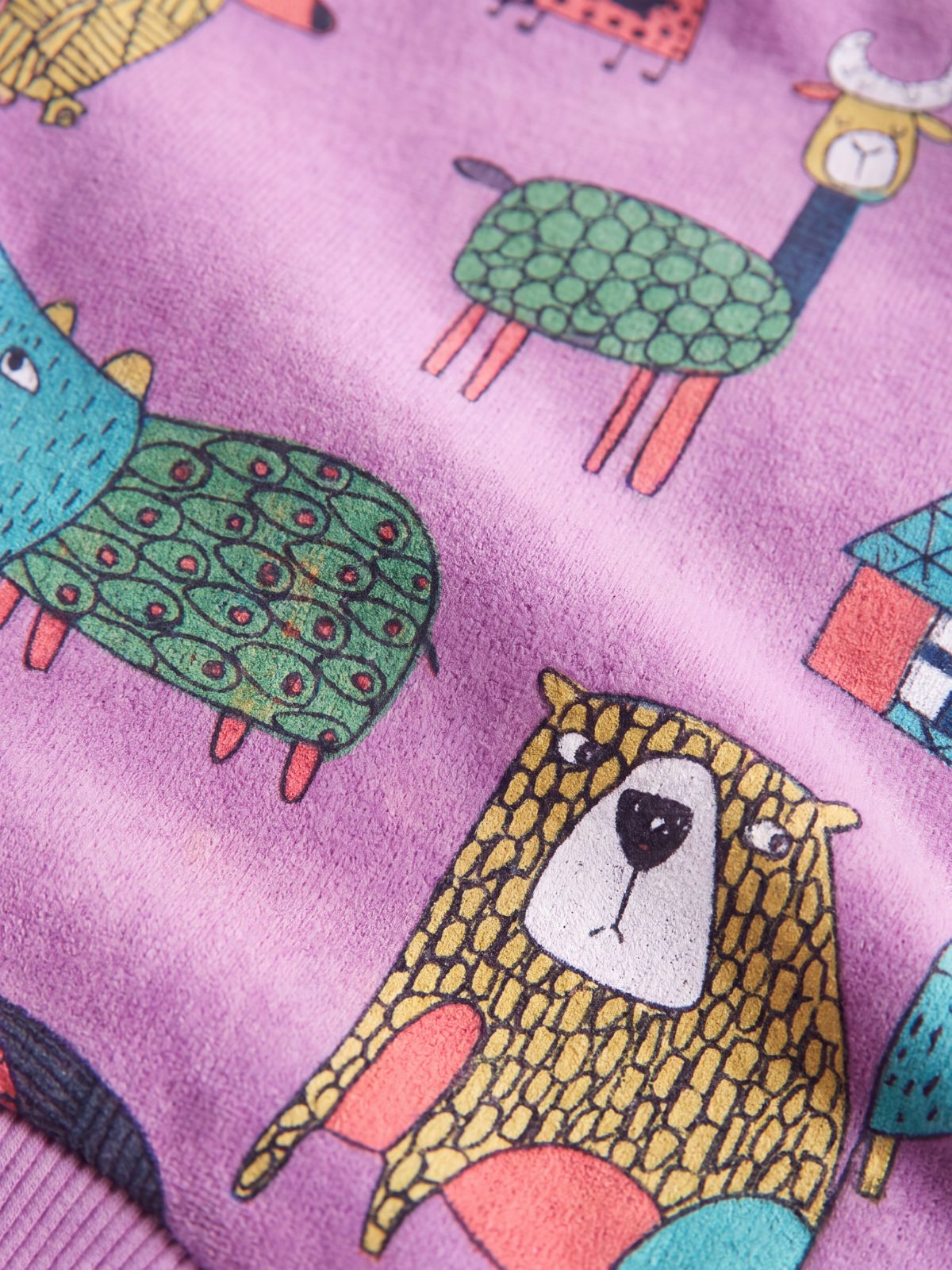 Gros plan sur l'imprimé d'animaux colorés du pull chien violet : ours, crocodile et petites maisons
