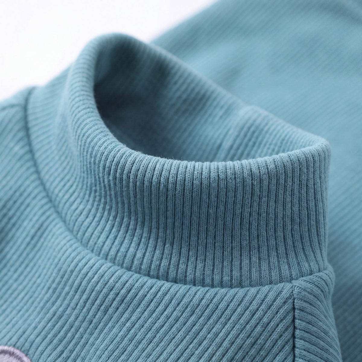 Gros plan sur le col montant du pull chien turquoise en maille lisse
