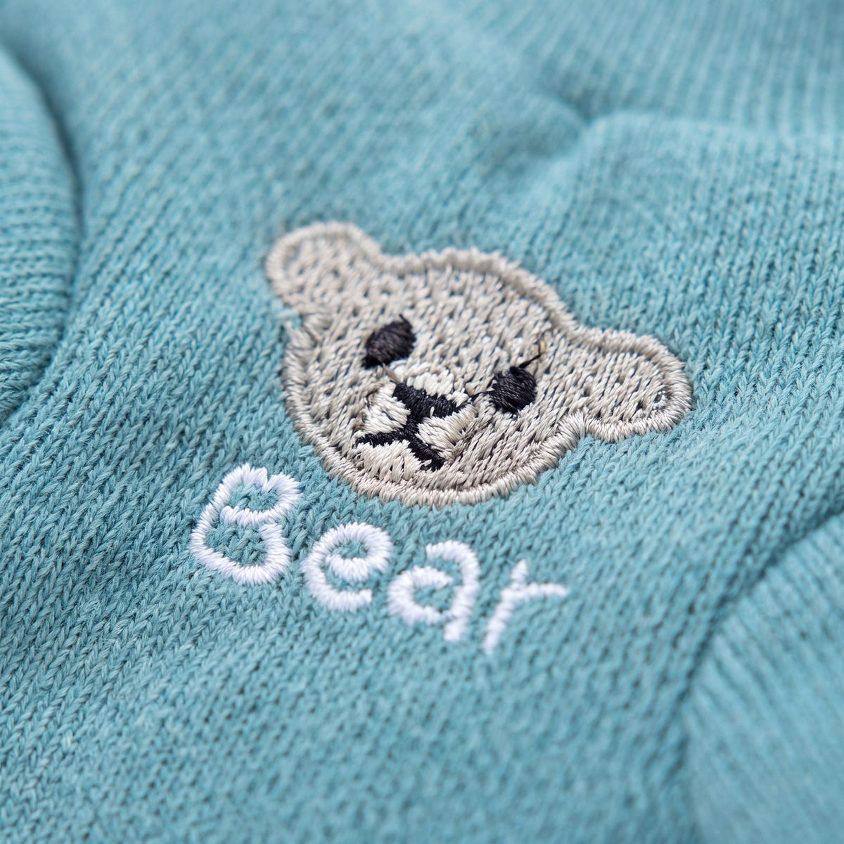 Gros plan sur le petit ourson brodé Bear du pull chien turquoise