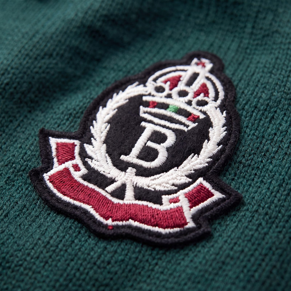 Gros plan sur l'écusson brodé du pull chien tricot style universitaire vert