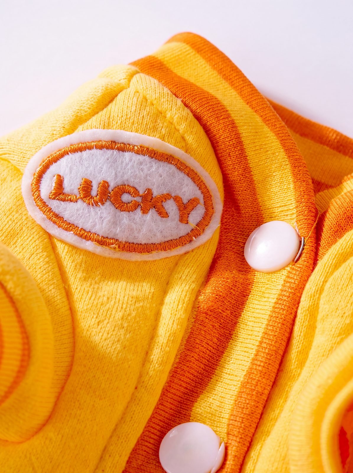 Gros plan sur l'écusson LUCKY brodé et les boutons-pression du pull jaune