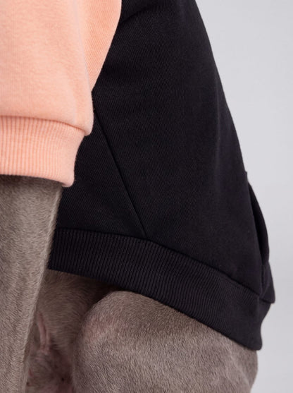 Gros plan sur le bas côtelé noir et la manche pêche du sweat à capuche chien color block